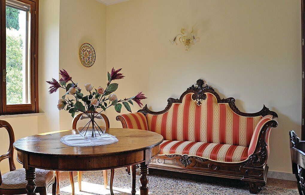 A room with a round wooden table, a striped sofa, and a vase of flowers.
