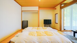 Une pièce de style japonais traditionnel, avec un sol recouvert de tatamis, un lit avec une literie blanche, une télévision et une porte coulissante donnant sur un balcon.