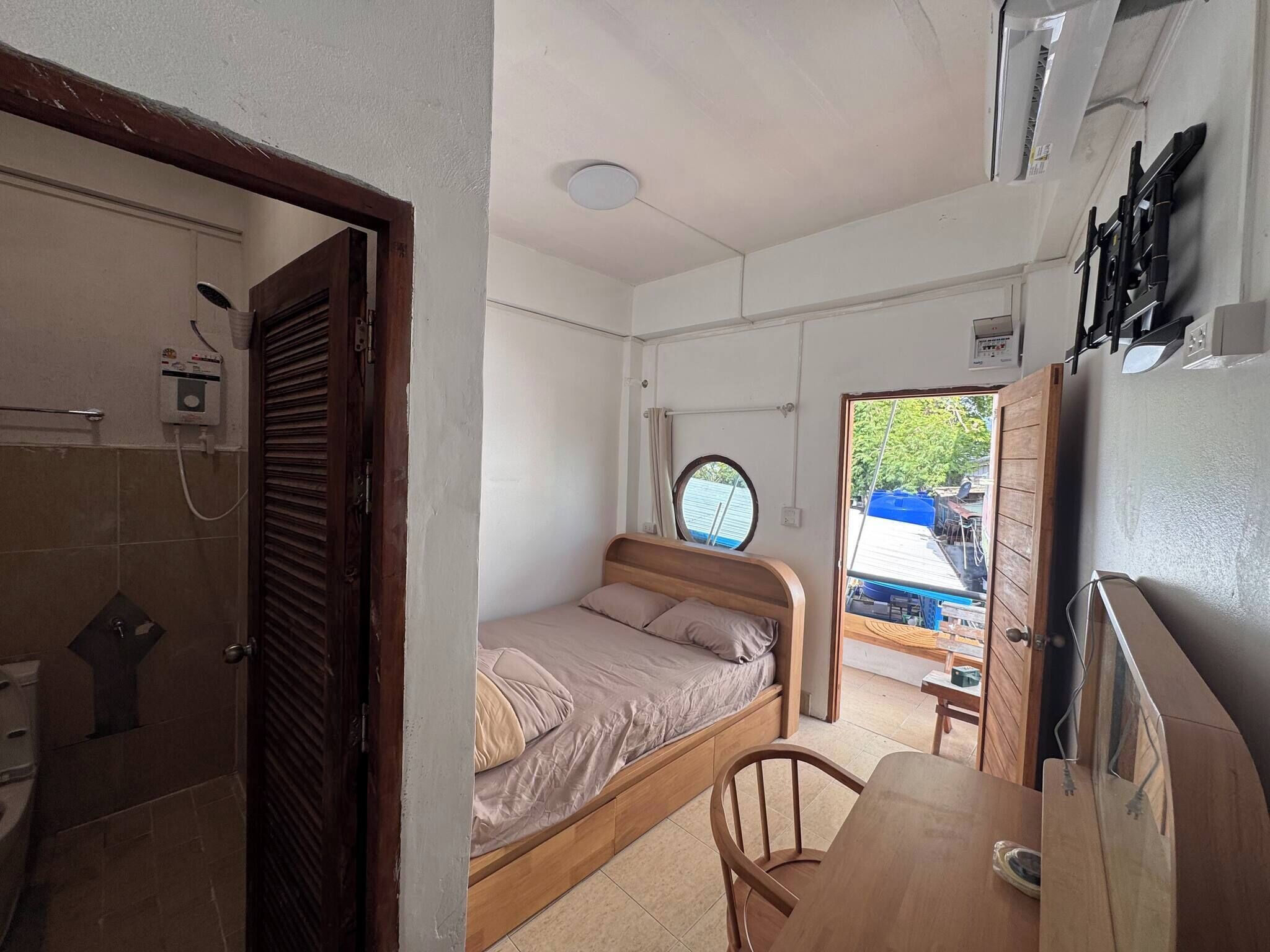 A compact room with a bed, a small table, a shower, and a window.