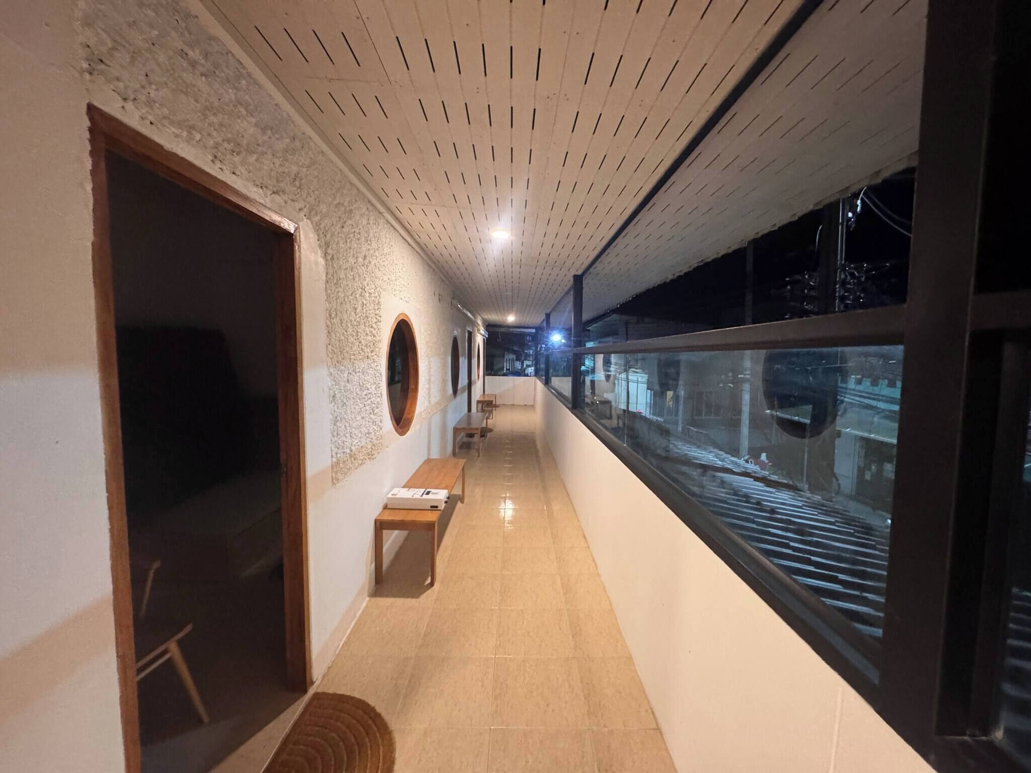 A corridor with a tiled floor, wooden benches, circular wall decorations, and a view through a glass window.