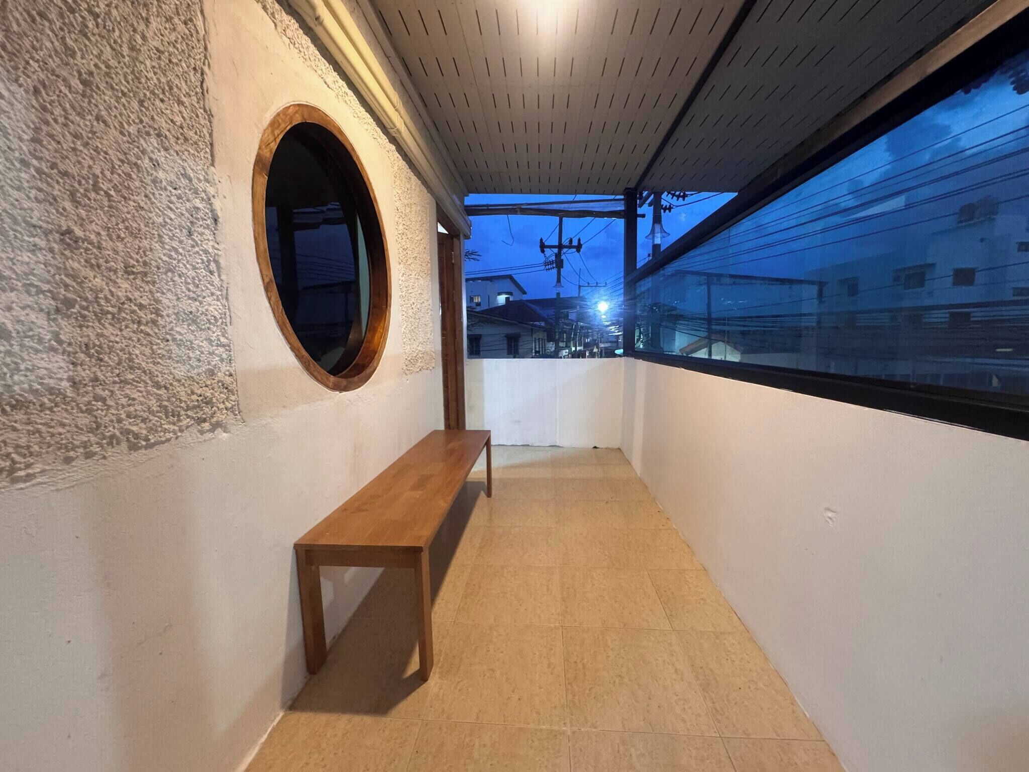 A corridor with a wooden bench, a round mirror, and a view of buildings through a window.