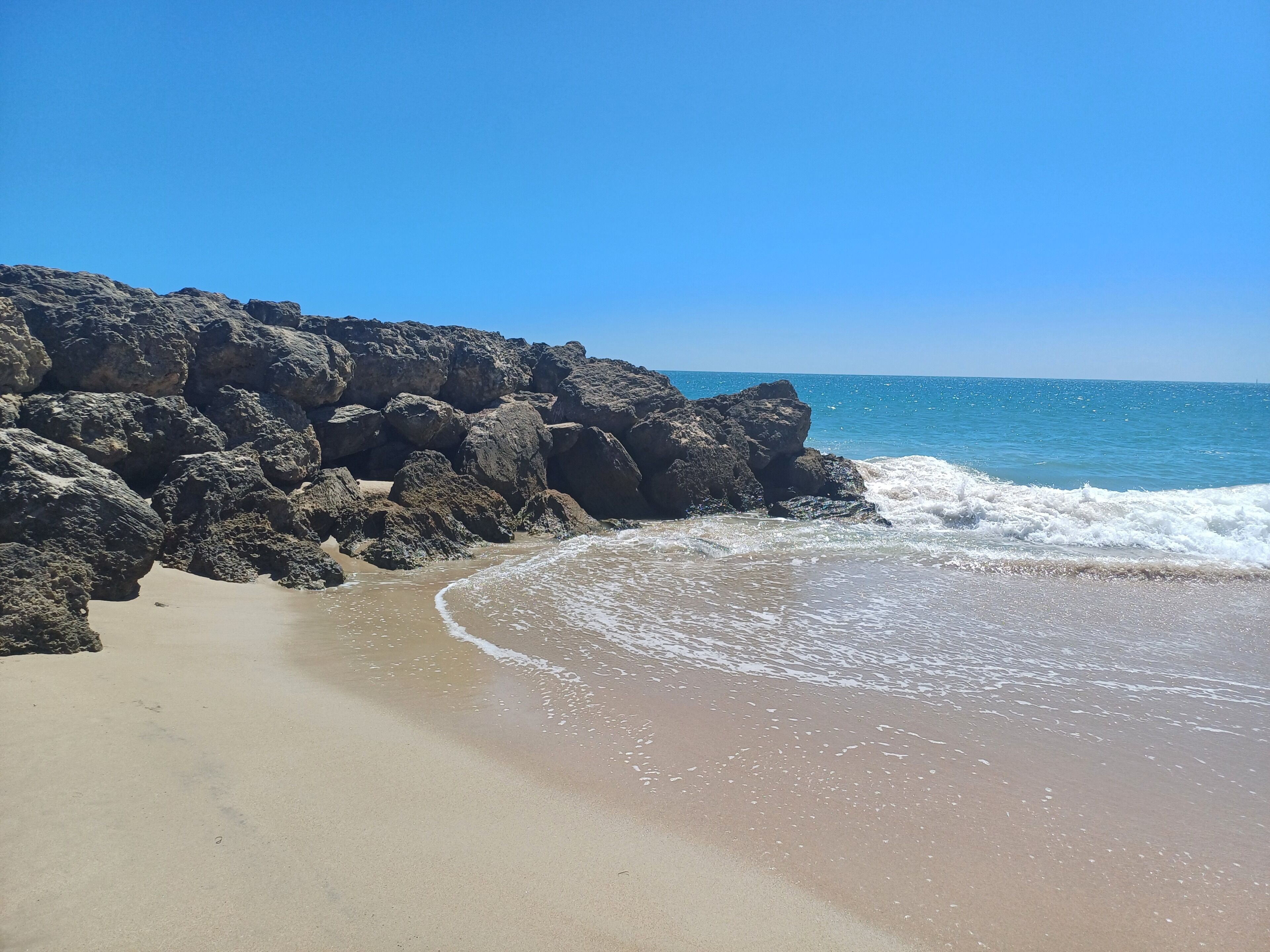 Ein Strand mit großen Felsen, sandigem Ufer und Wellen.