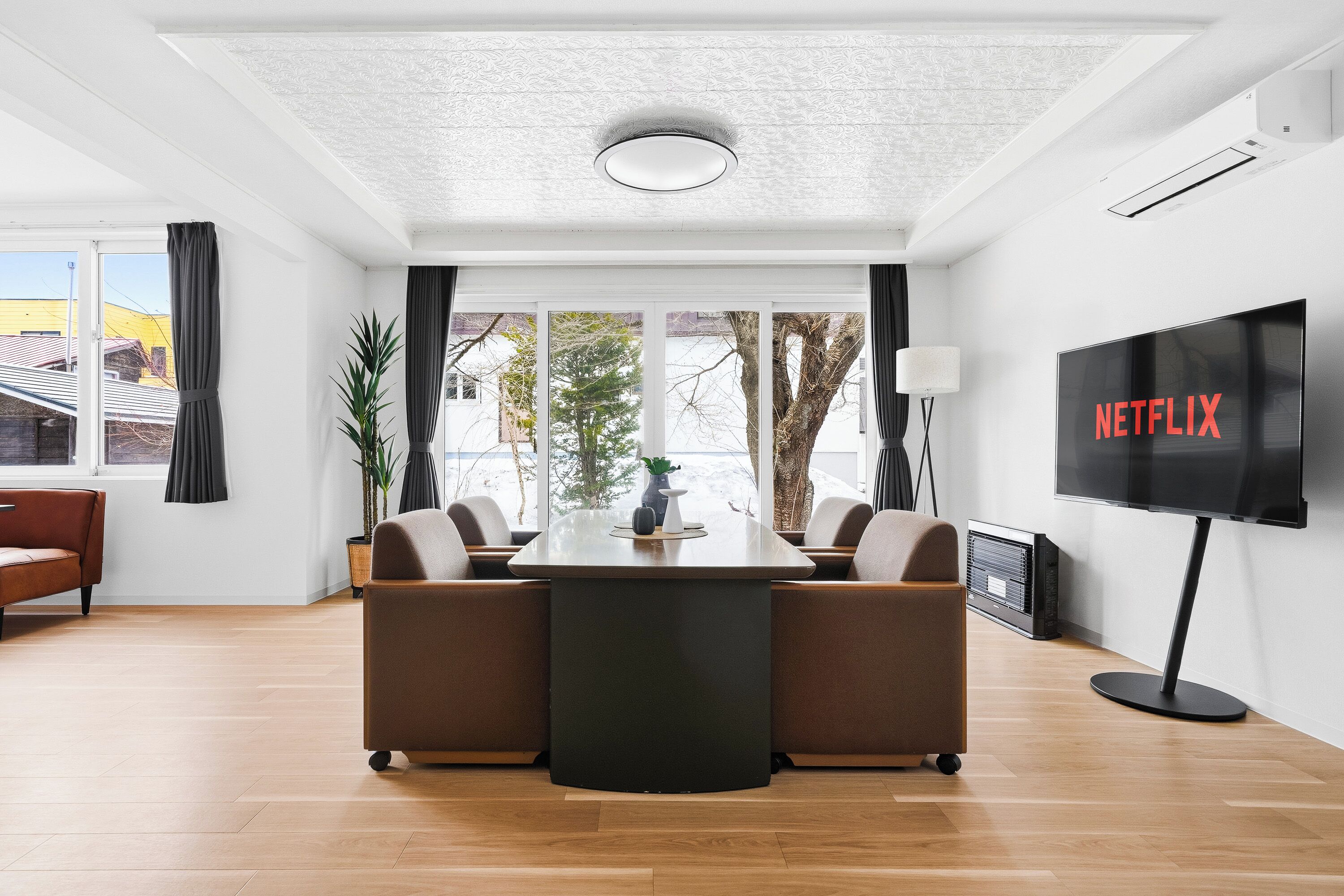 A modern living room with a central table, sofas, a TV, and large windows.