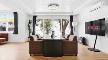 A modern living room with a central table, sofas, a TV, and large windows.