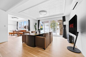 A modern living room with a dining area, large windows, and a flat-screen TV mounted on the wall. - NORD BIRCH (Tobetsu)