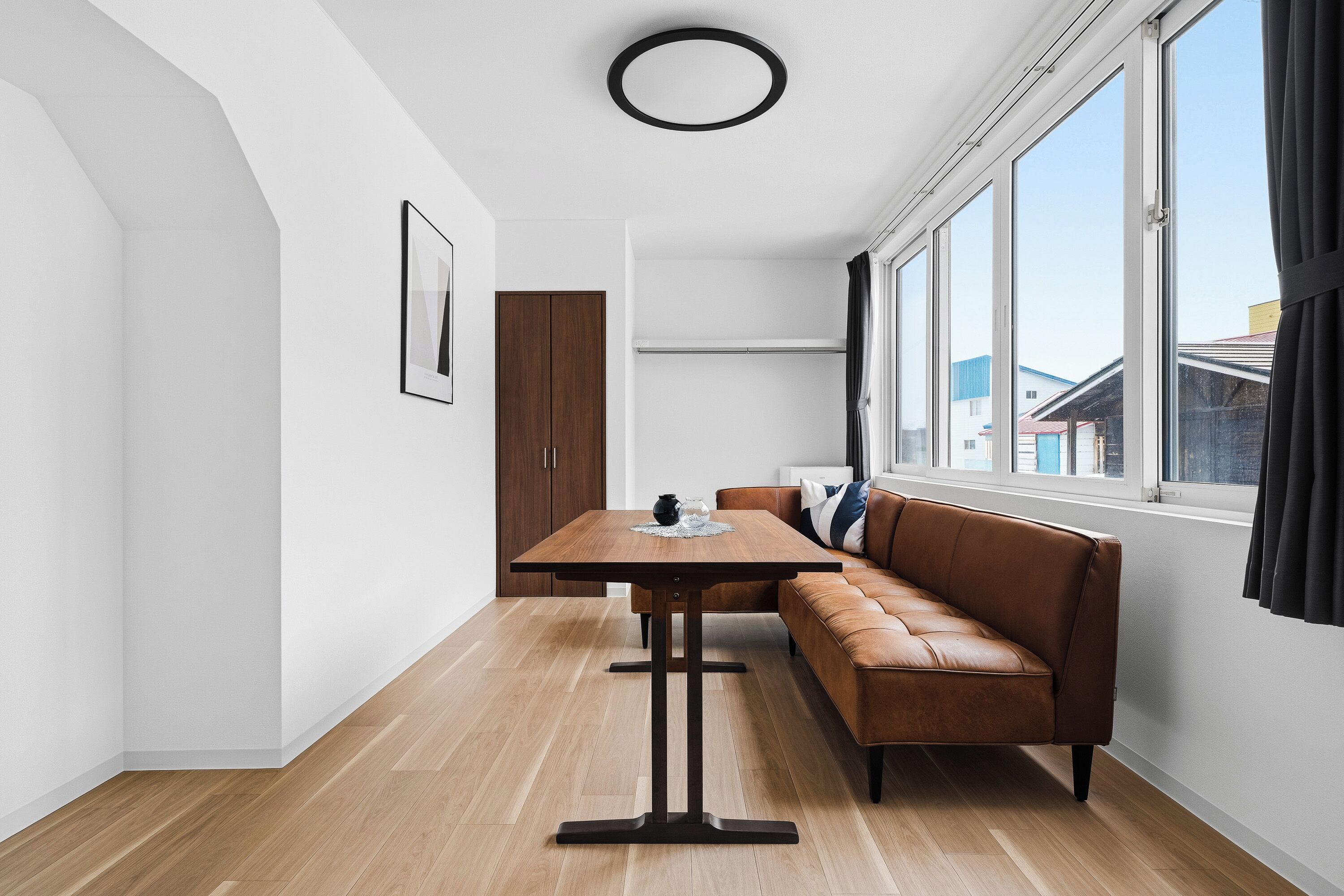 Een moderne eetruimte met een houten tafel, een bruine leren bank en een groot raam met gordijnen.