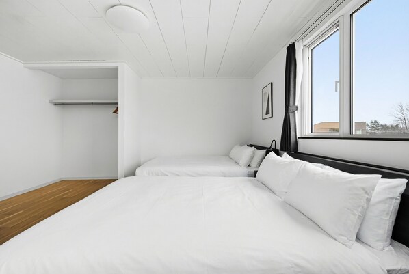 A room with two beds, a wooden floor, a white ceiling, and a window with a view of buildings. - NORD BIRCH (Tobetsu)