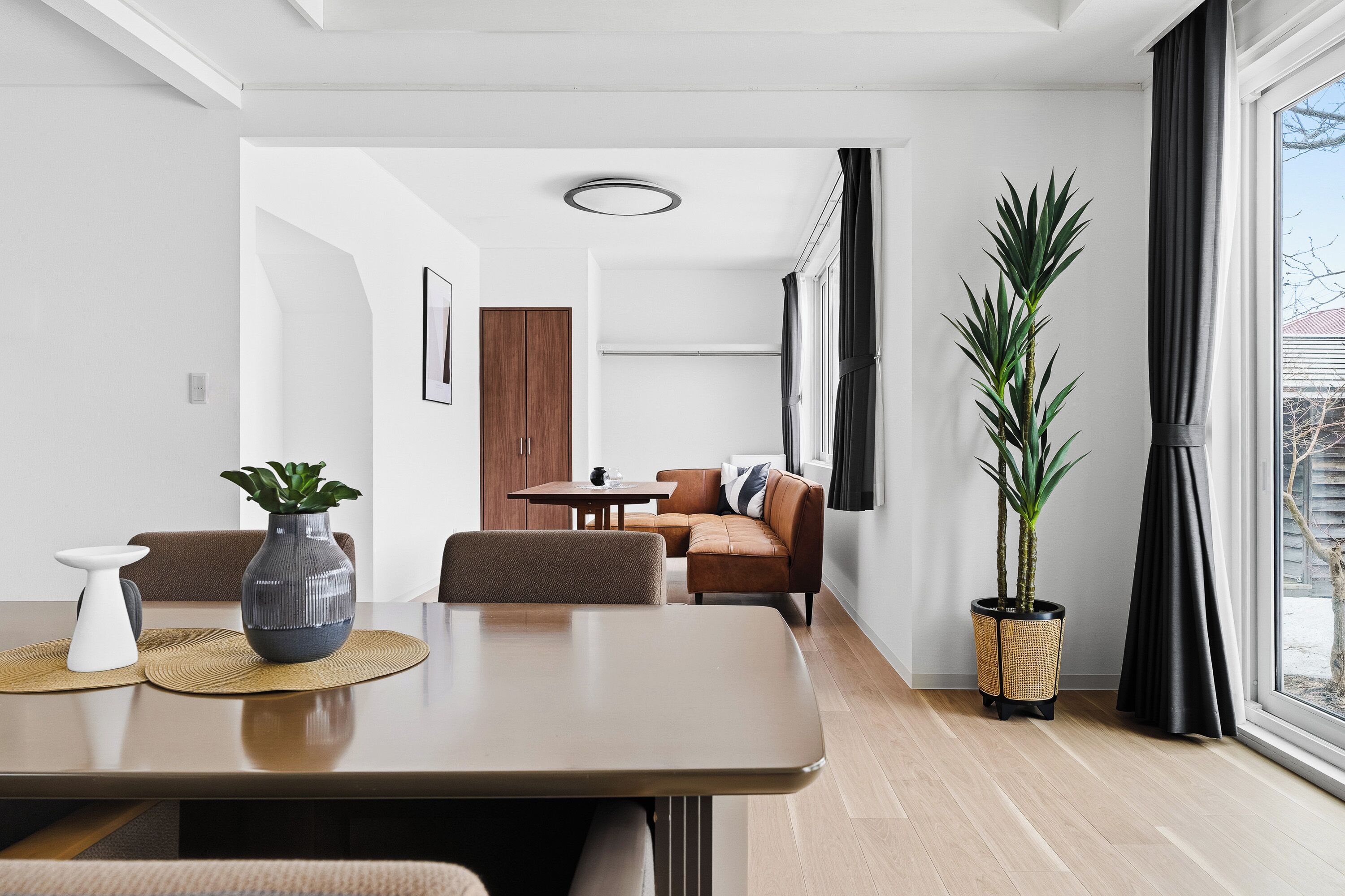 A modern living room with a dining table, sofa, and potted plants.