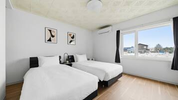 A hotel room with two beds, a ceiling with a geometric pattern, an air conditioning unit, and a window with a view of buildings.