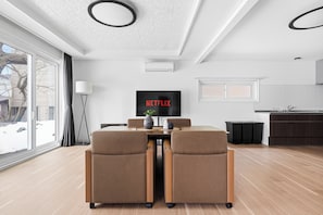 A modern living room with a dining table, two chairs, a TV, and a kitchen area.