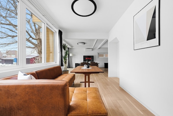 A modern living room with a large window, a sofa, a dining table, and a TV.