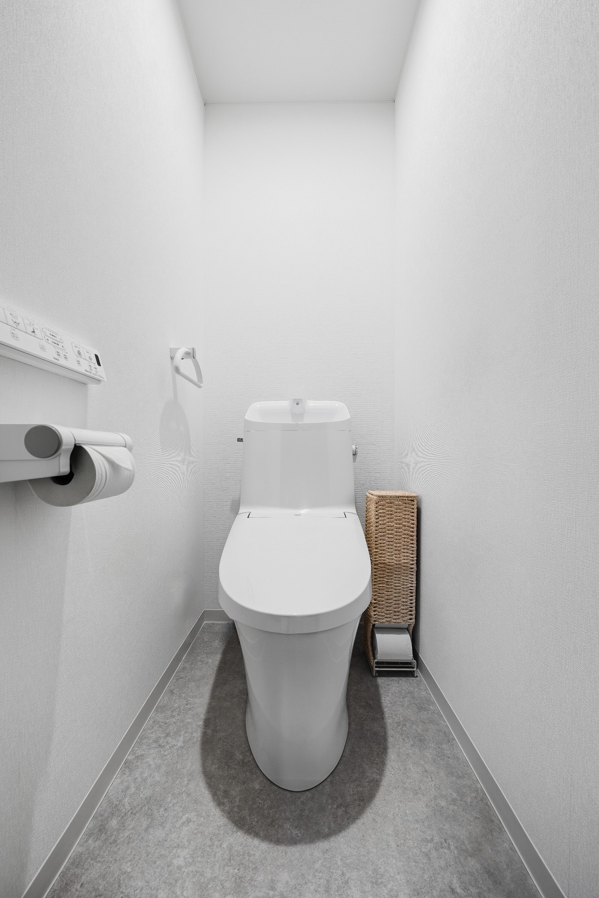 A modern bathroom with a toilet, toilet paper, and a wicker basket.