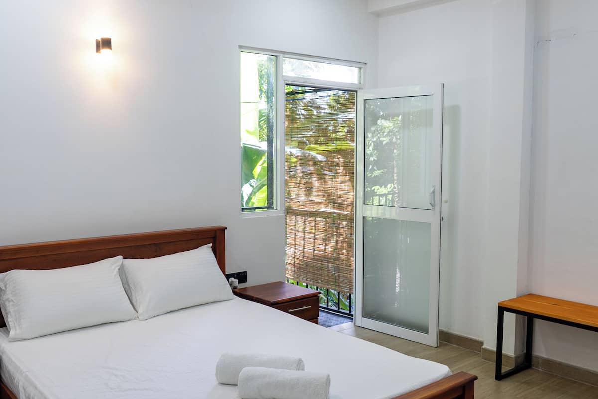 Ein Schlafzimmer mit einem hölzernen Bett, einem Nachttisch, einer Bank und einer Schiebetür zu einem Balkon.