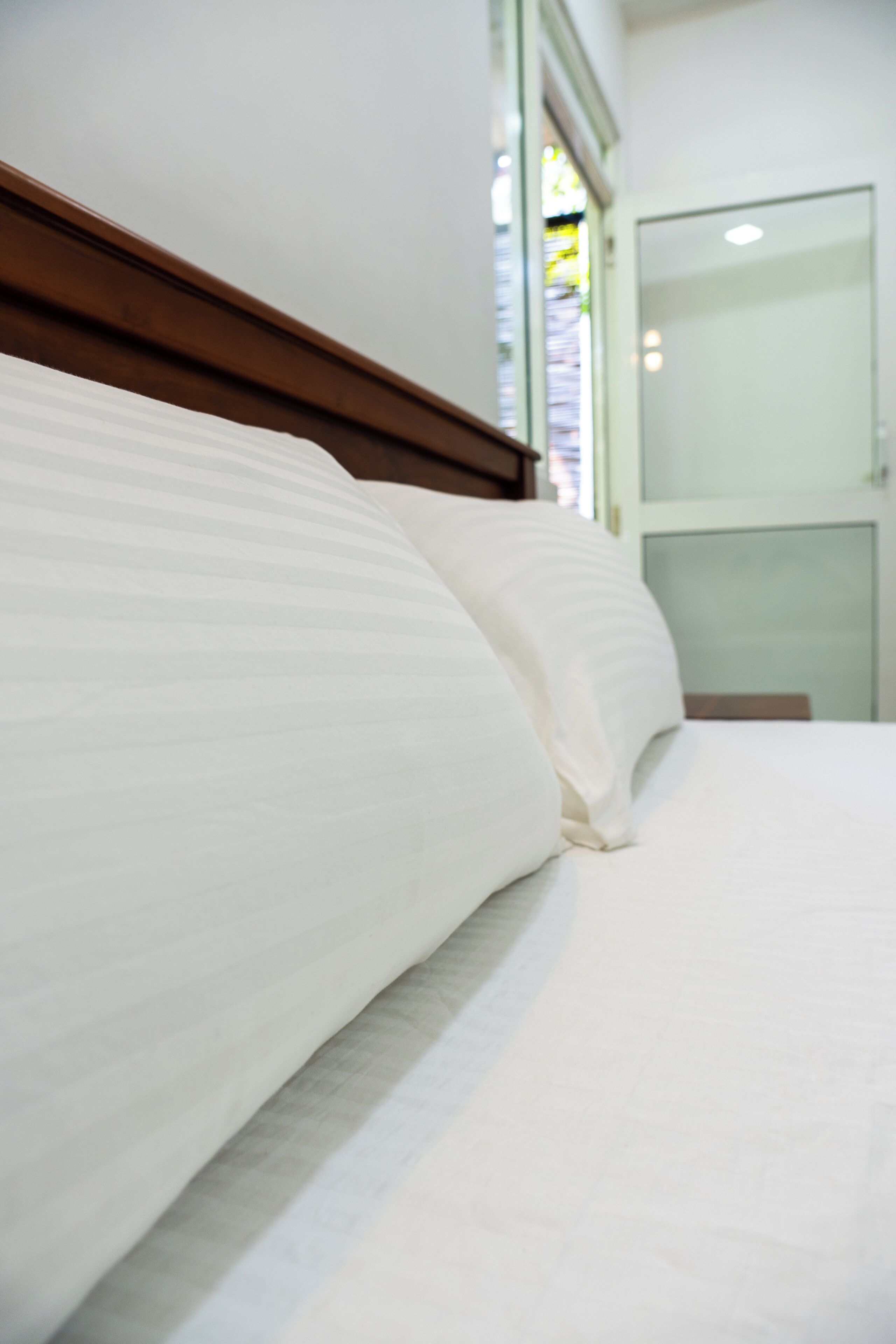 Cama bem arrumada com lençóis brancos e cabeceira de madeira em quarto de hotel.