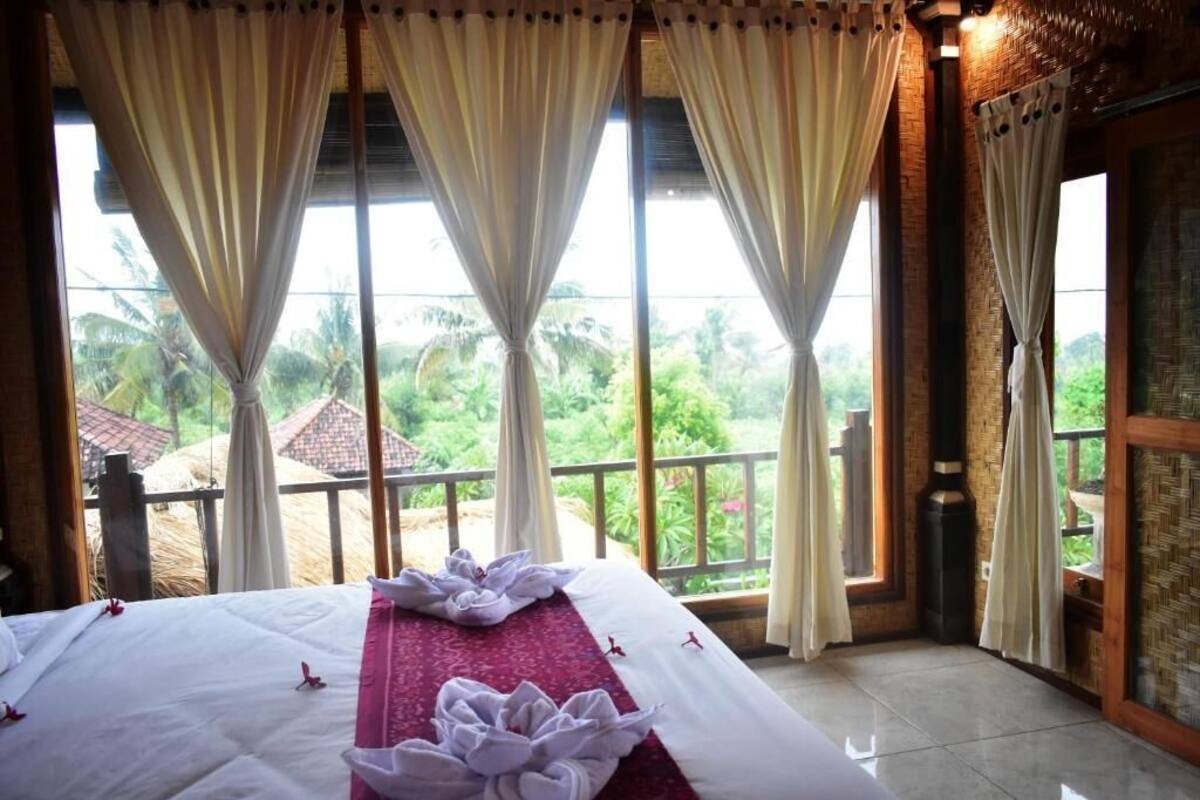 A room with a bed, large windows, and a view of greenery.