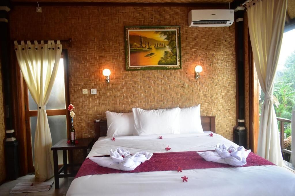 A hotel room with a bed, a painting, an air conditioner, and a window with curtains.