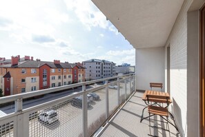 A balcony with a table and chairs, overlooking a street with parked cars and buildings. - Modern Apartment | Gdansk | Balcony | Parking (Gdańsk)
