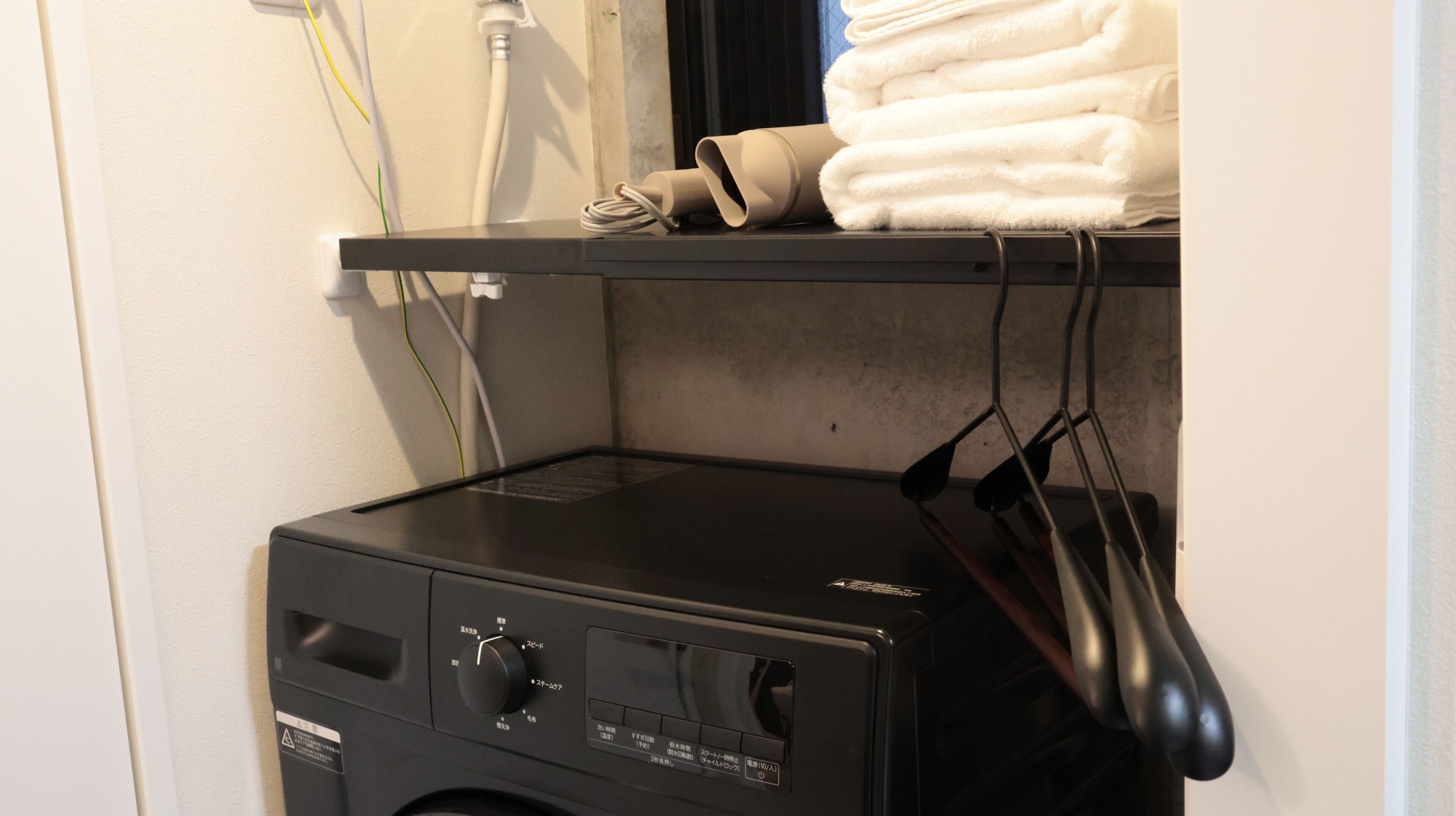 A washing machine with a control panel, a shelf with folded towels, and a window with a view.