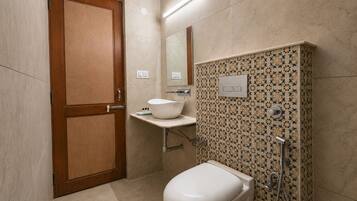 Baño con puerta de madera, lavamanos blanco, inodoro y ducha con revestimiento estampado.