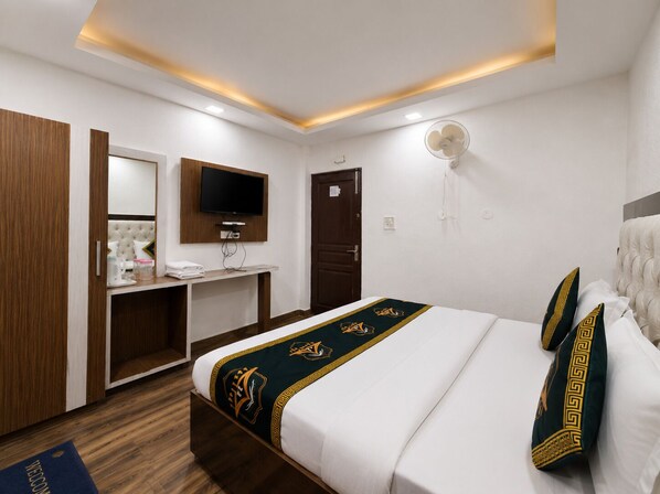 A hotel room with a bed, a TV mounted on the wall, a desk, and a wardrobe. - Kavin Highland - The Mall (Dalhousie)