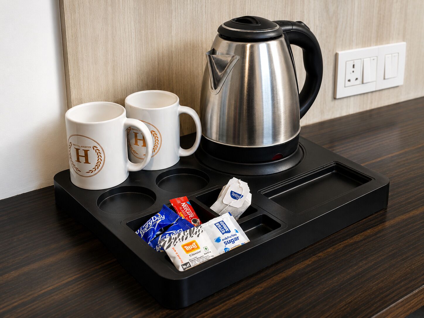 Una cafetera, dos tazas y una bandeja con sobres de azúcar y una bolsita de té sobre una superficie de madera.