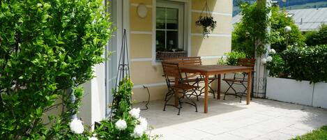 A patio with a table and chairs, a hanging planter, and a window with a view of the mountains.