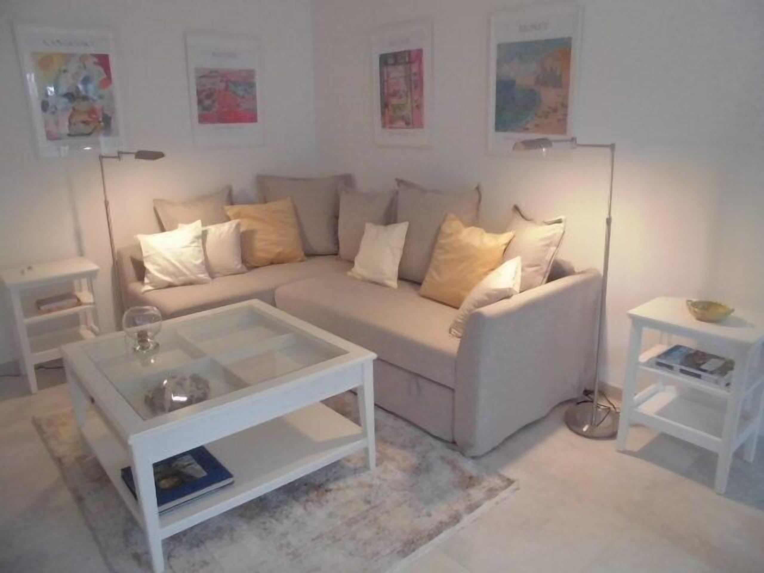Una sala de estar con un sofá color beige, una mesa de centro blanca y una lámpara de pie.