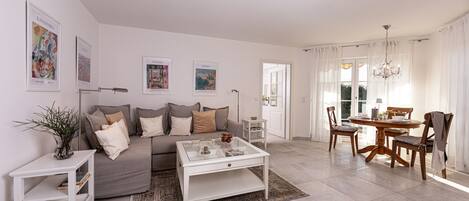 A modern living room with a grey sofa, white coffee table, and a dining area with a wooden table and chairs.