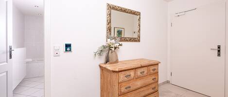 Un baño con azulejos blancos, un aparador de madera con cajones, un espejo con marco decorativo y una puerta con picaporte.
