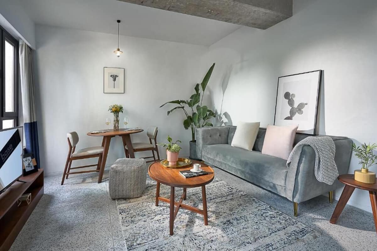 Una sala de estar moderna con un sofá gris, una mesa de centro, una mesa de comedor con sillas, un televisor y una planta grande.