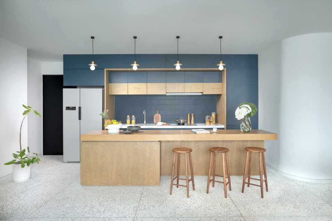 Eine moderne Küche mit einer zentralen Kochinsel, Barhocker, Pendelleuchten und einer Spritzschutzwand.