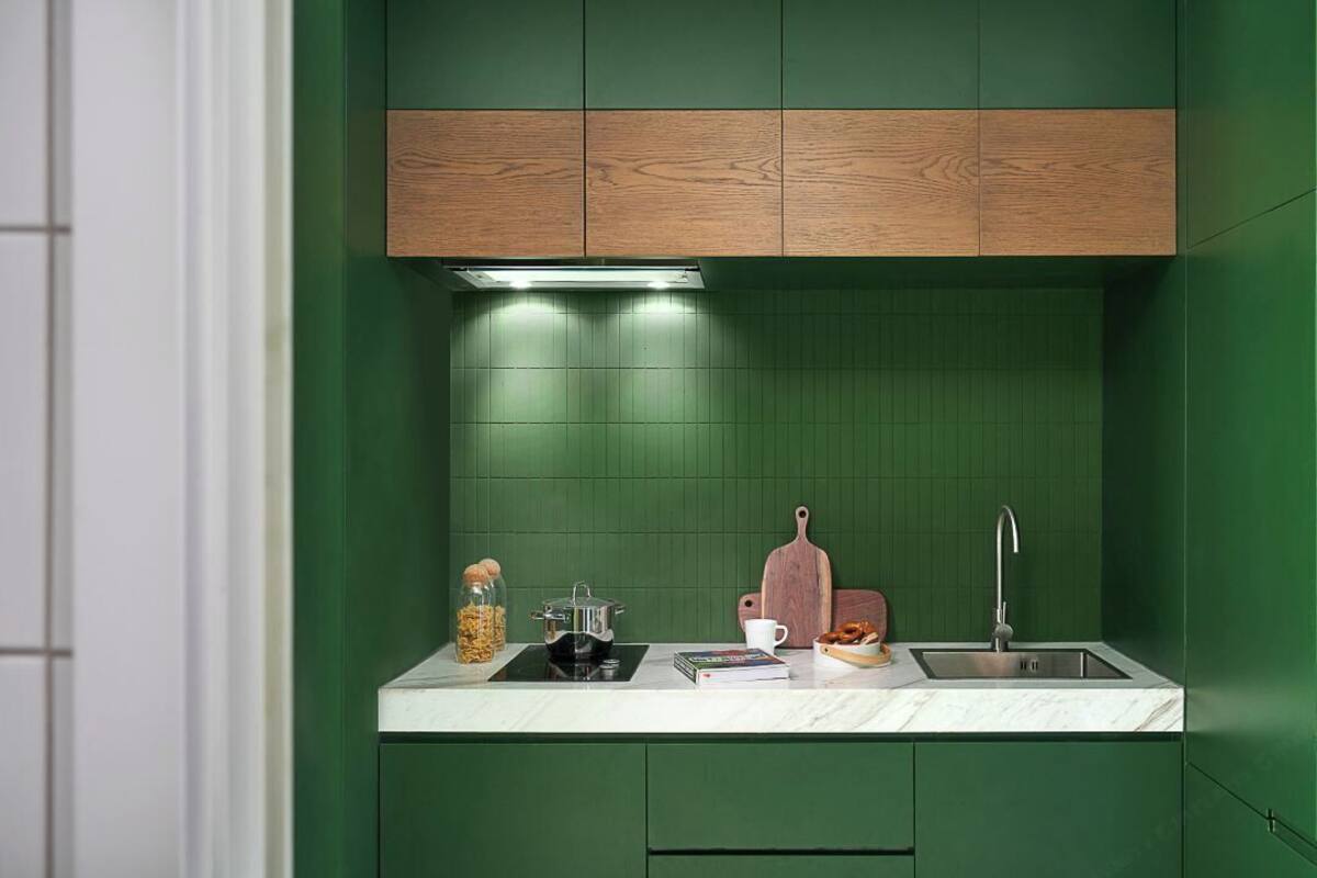 Una cocina con gabinetes verdes, encimera blanca, pileta de acero inoxidable y tabla de cortar de madera.
