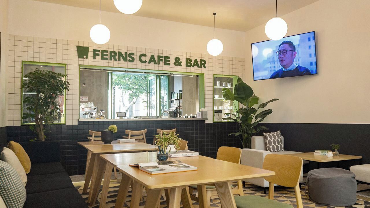 A cozy cafe with tables and chairs, a TV mounted on the wall, and a green sign above the counter.
