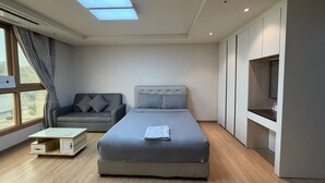 Un dormitori modern amb un llit, un sofà, una televisió i una finestra amb cortines.