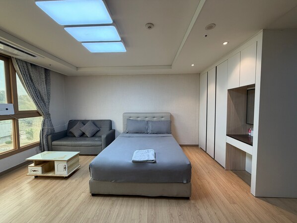 A modern bedroom with a bed, a sofa, a TV, and a window with curtains.