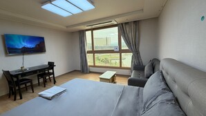 Habitació d'hotel amb llit, escriptori amb cadires, sofà, televisió penjada a la paret i finestra gran amb cortines.