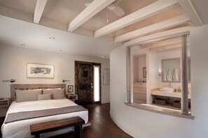 Een slaapkamer met een bed, een houten hoofdbord, een groot raam en uitzicht op een badkamer.