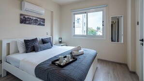 Ett modernt sovrum med en säng, ett fönster, en luftkonditionering och en tavla som föreställer en stadsbild.