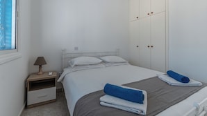 A bedroom with a bed, a nightstand, a lamp, a wardrobe, and a window. - Beach Escape Apartment (Pyla)