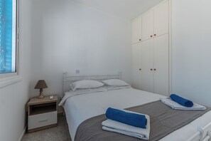 A bedroom with a bed, a nightstand, a lamp, a wardrobe, and a window. - Beach Escape Apartment (Pyla)