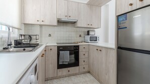 A modern kitchen with wooden cabinets, a stainless steel refrigerator, a microwave, and a dishwasher. - Beach Escape Apartment (Pyla)