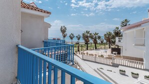 A balcony with blue railings overlooking a pool area, palm trees, and a clear sky. - Beach Escape Apartment (Pyla)