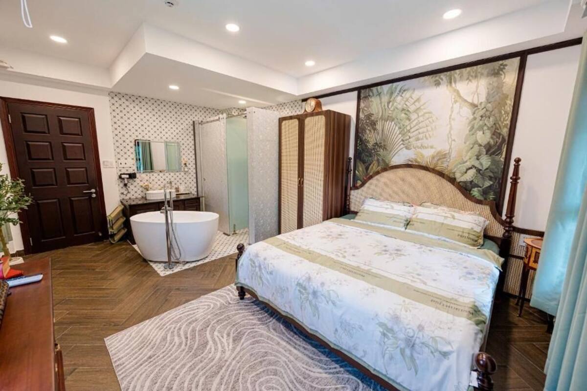 A bedroom with a large bed, a bathtub, a mirror, and a door.