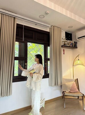 A room with a window, curtains, a chair, a lamp, and a shelf with books. - The ChiMi Homestay & Coffee (TP. Ho Chi Minh)