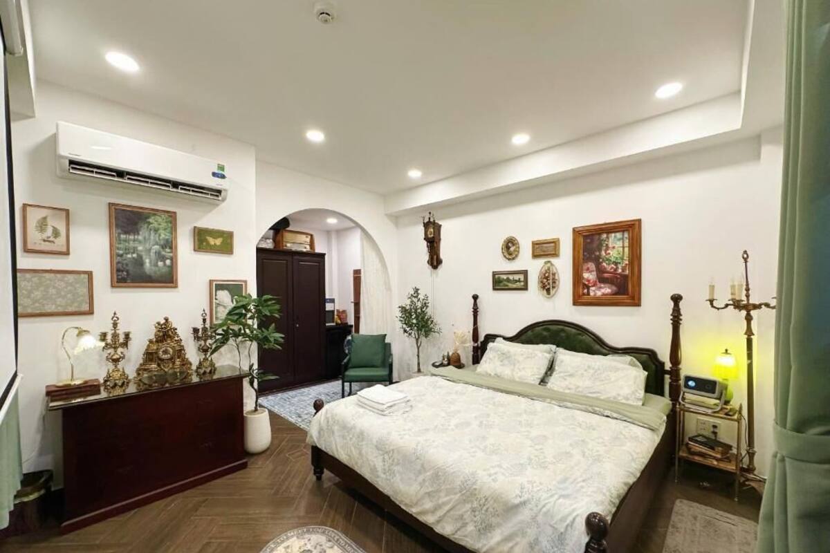A bedroom with a bed, bedside table, lamp, wall art, and a desk with a chair.