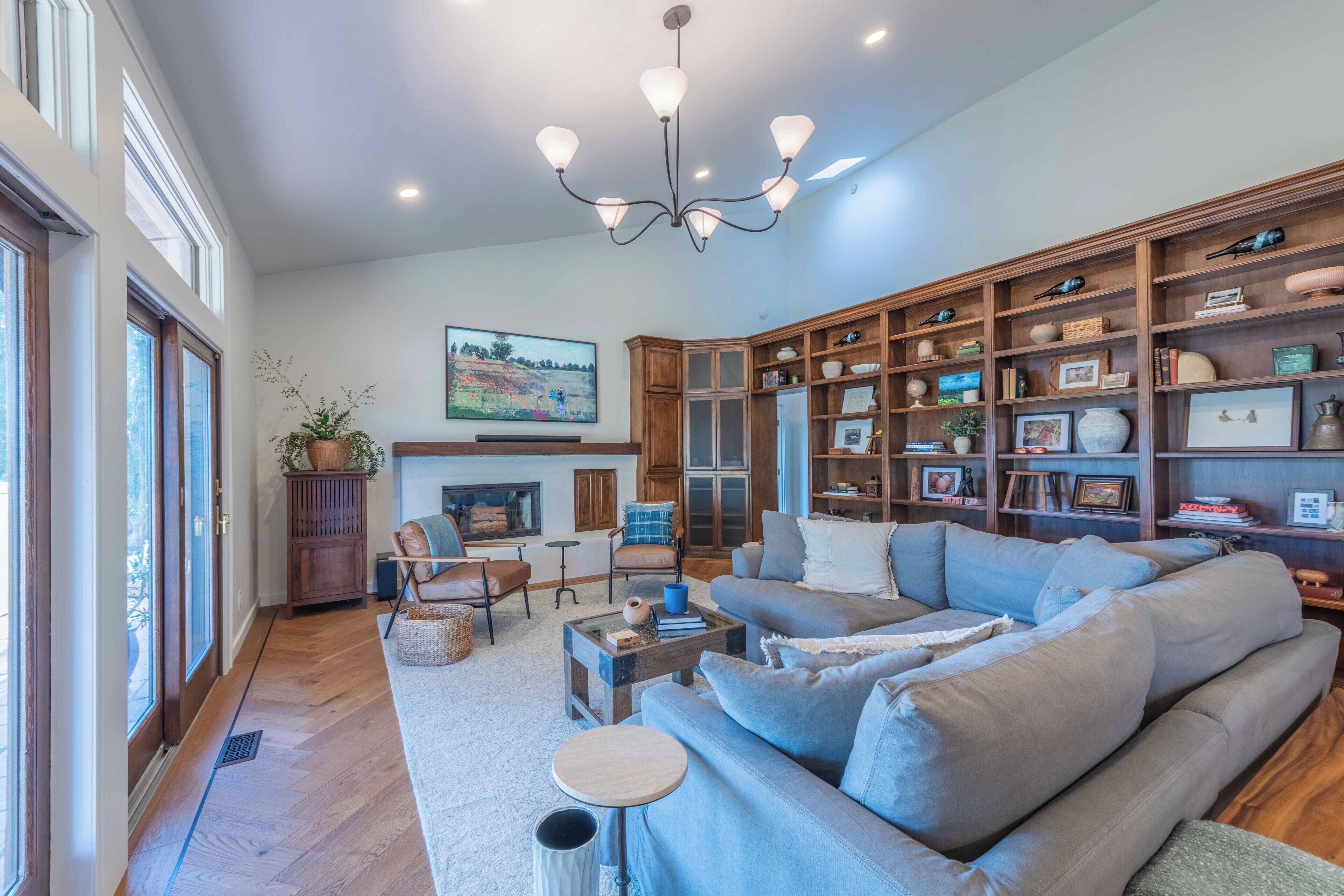 A spacious living room with a large sectional sofa, a fireplace, a wooden bookshelf, and a chandelier.