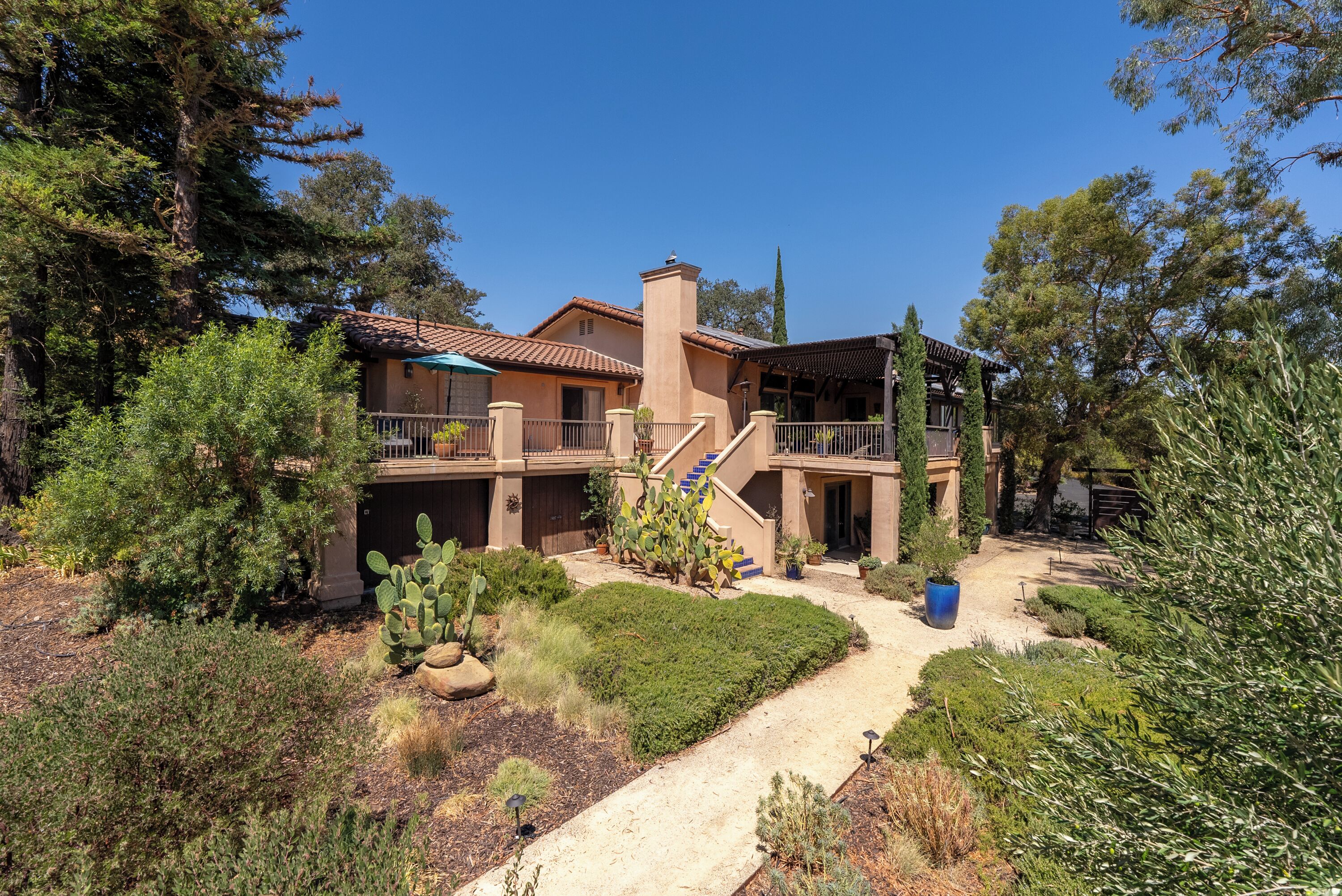 Ein zweigeschossiges Haus mit Terrasse, Treppe und einem Garten mit verschiedenen Pflanzen.
