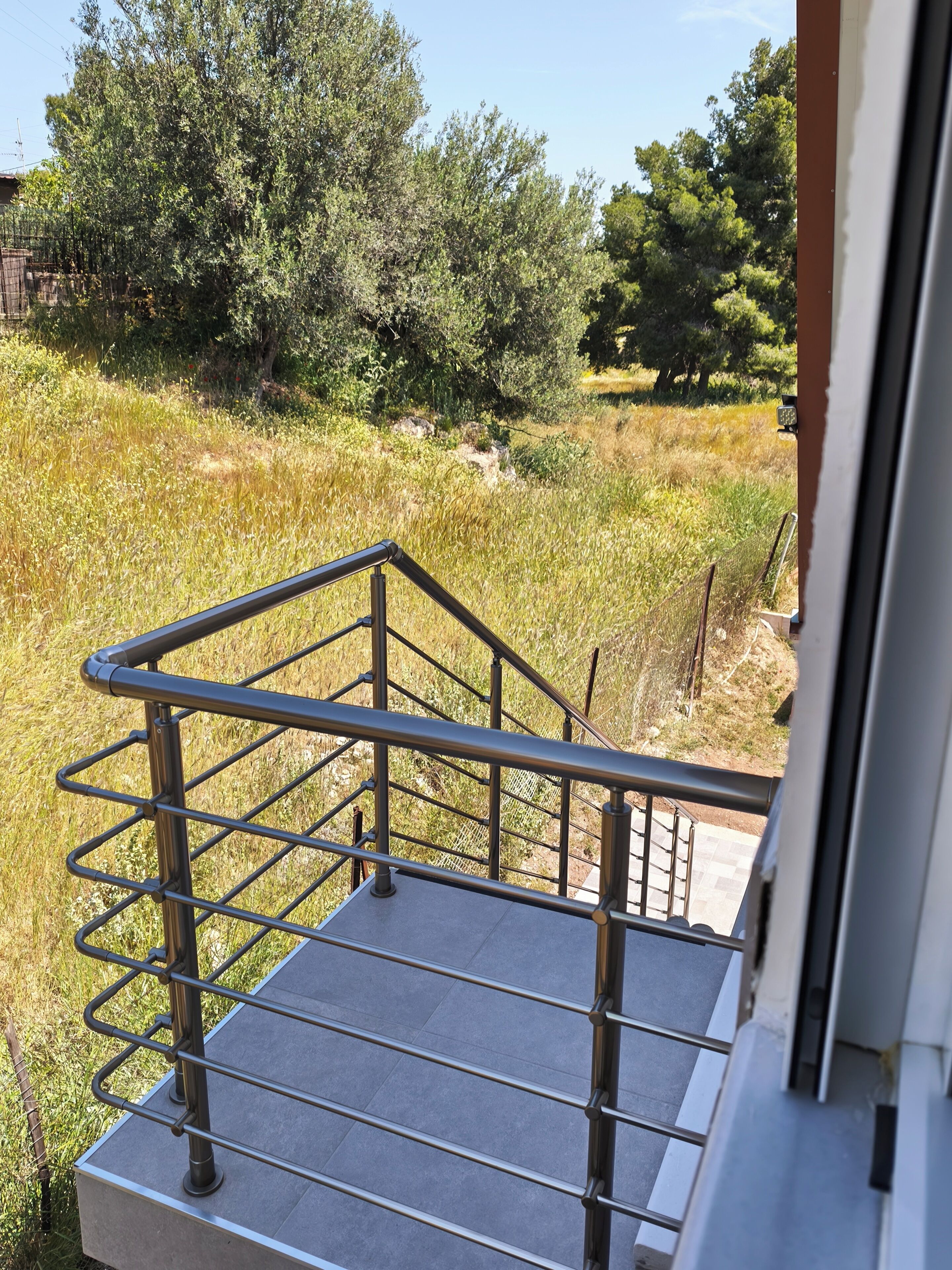 A metal staircase leading to a balcony with a view of a grassy field and trees.