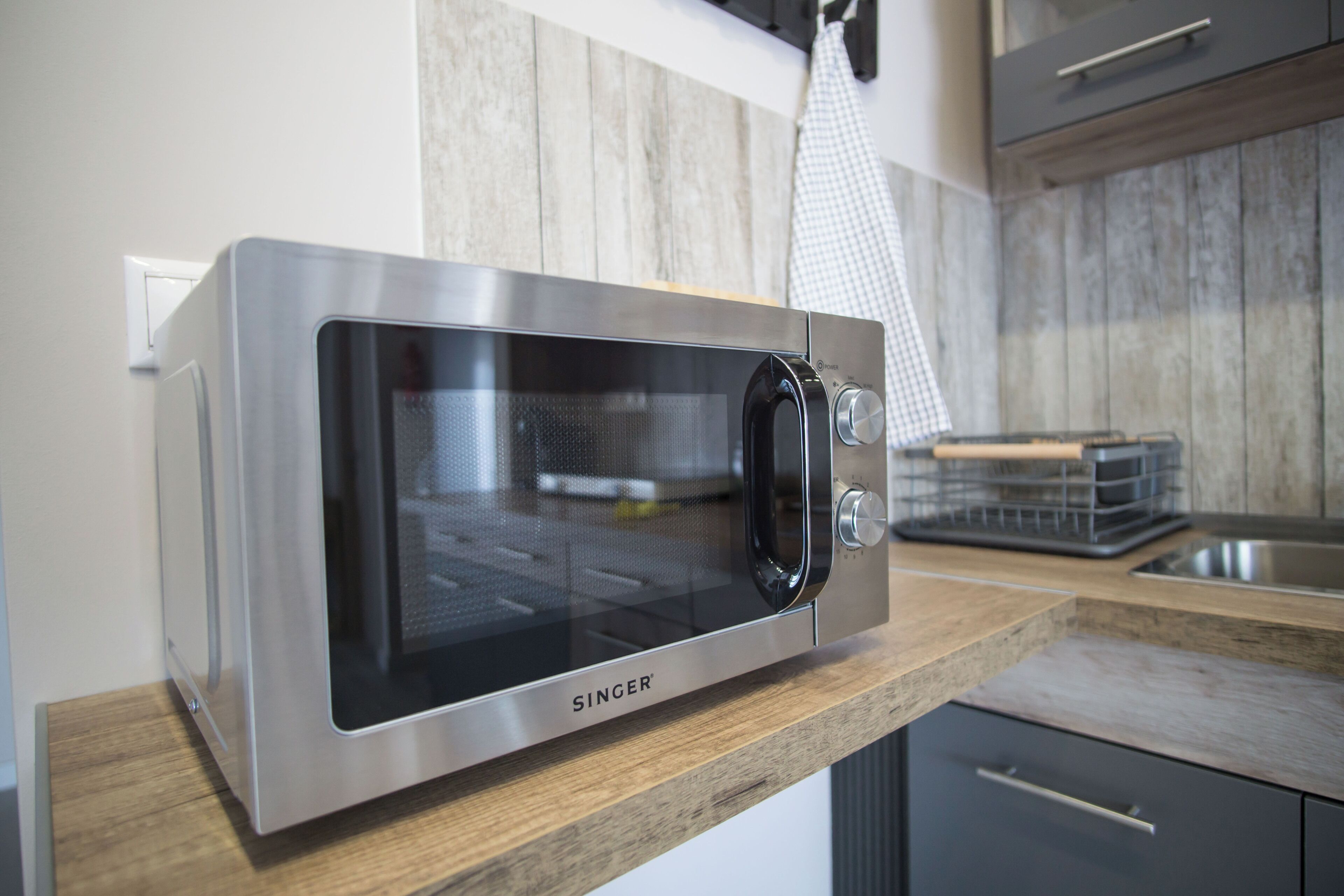 A stainless steel microwave oven on a wooden countertop in a kitchen.