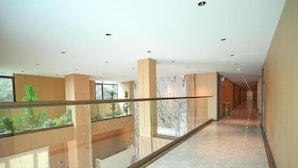 Interior de un hotel moderno con barandilla de vidrio, suelo de mármol y vistas a zonas verdes.